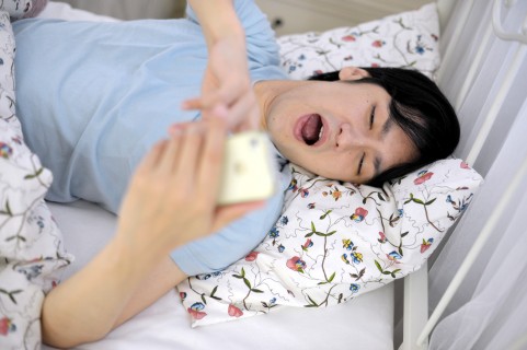 スマホを見て眠りにつく男の写真