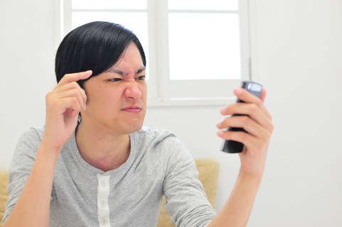 スマホを眺めて怒っている男の人の写真