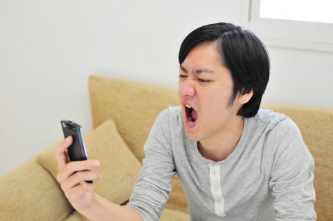 誤タップ狙ってるサイトはウザイですね。 スマートフォンを見て怒っている男の人の写真