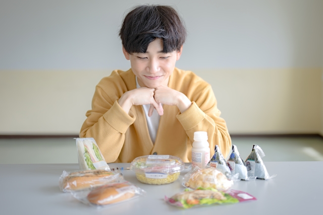 たくさんの食べ物を並べてどれから食べるかを迷っている若い男性