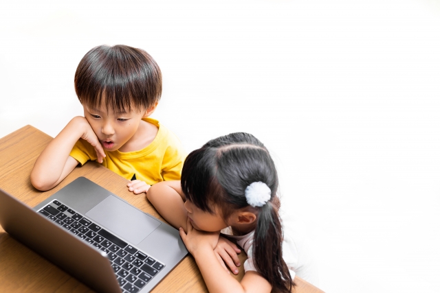 3~4歳くらいの兄妹がオンライン英会話を一緒にパソコン画面を見ながらやっている画像