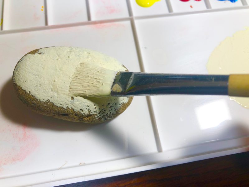 石に絵筆で白い絵の具を塗る様子を撮影した写真