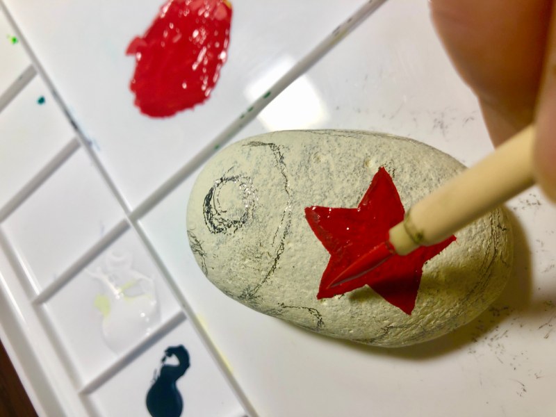 石の表側に絵筆を使って着色する様子を撮影した写真