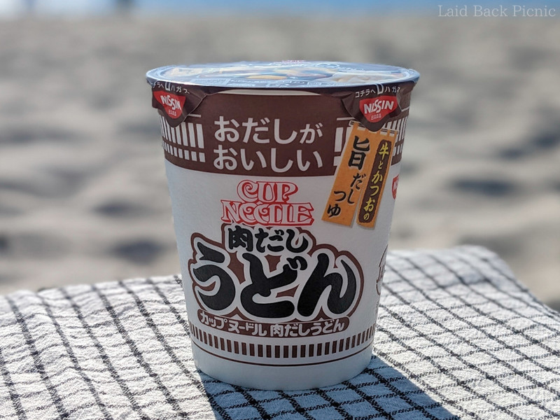 ピクニックのミニテーブルに乗せたカップヌードル 肉だしうどん