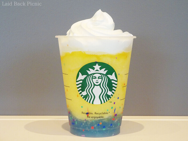 カップ底には水色のゼリー、その上に黄色いフラペチーノ、トッピングに白いホイップ。