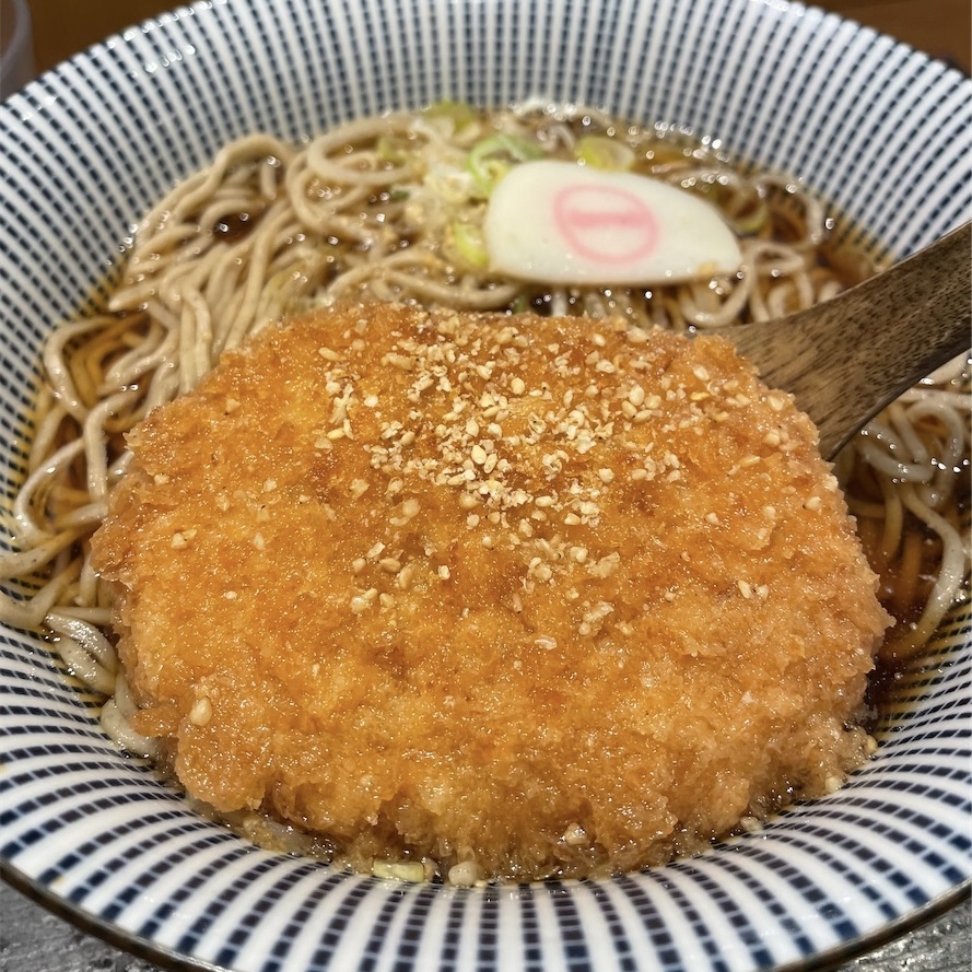 里芋コロッケそば、コロッケをレンゲで持ち上げた写真