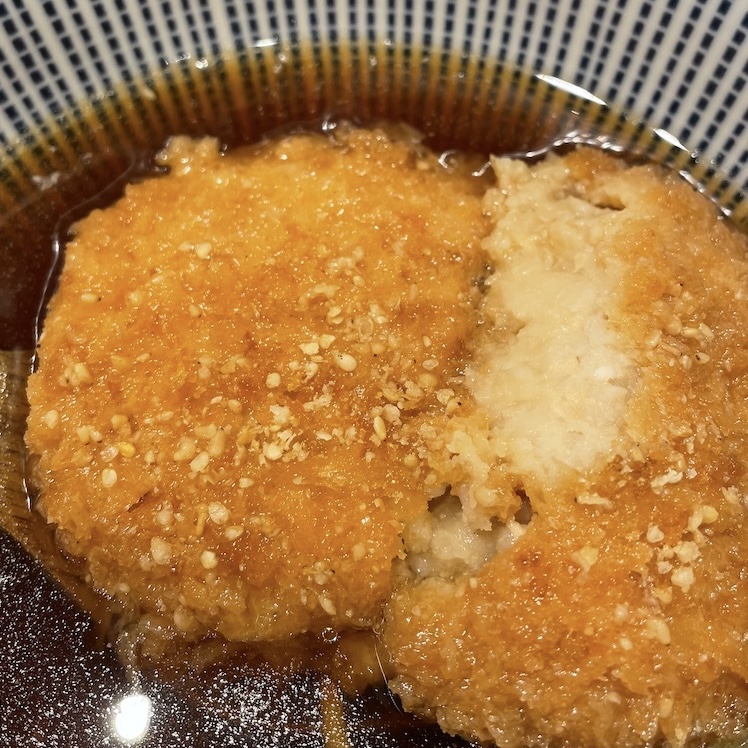 箸で半分に切ったつゆに浮かぶ里芋コロッケの写真