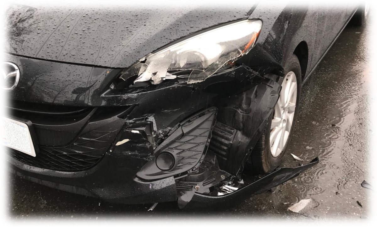 路上駐車中に事故で大きく損傷した車の写真。ヘッドライトやフロント部分、タイヤ周辺が破損し走行不能になった状態