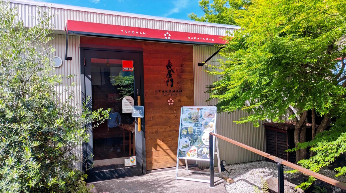 赤いひさしと木のドアが目印のたこまん長屋門さん外観。緑に囲まれて季節感たっぷりです