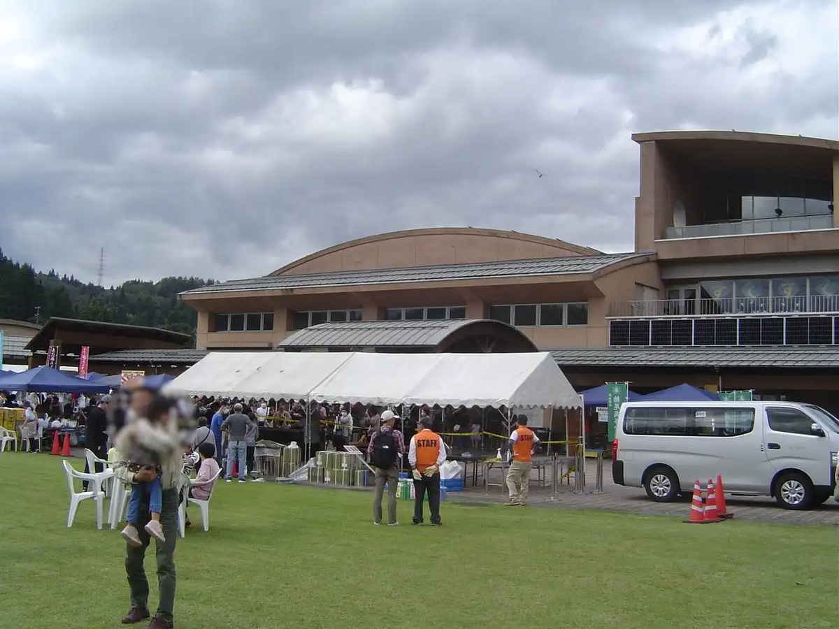 曇天の中、人々でにぎわう栃尾あぶらげ祭りの会場、栃尾産業交流センターおりなすの様子。