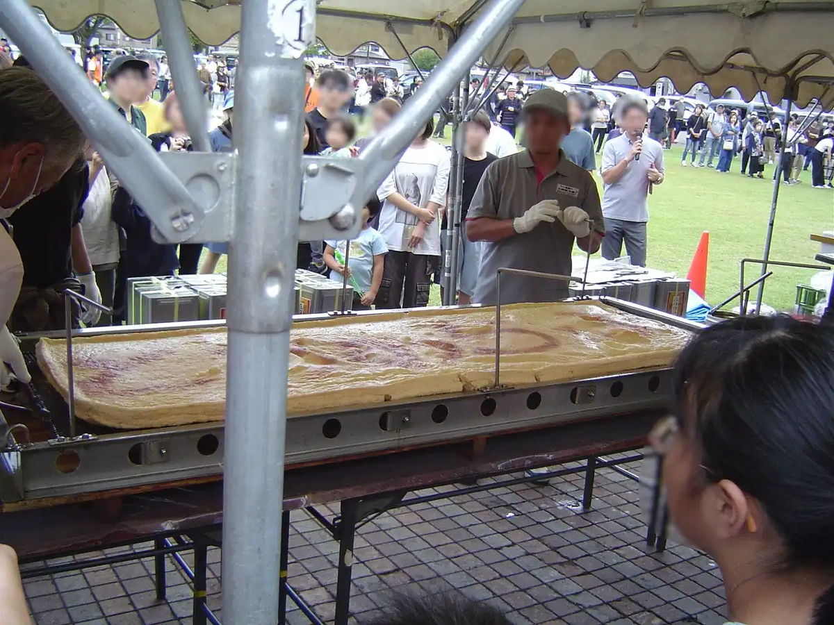 超巨大あぶらげが揚げ上がり、まな板の上にのせられている様子