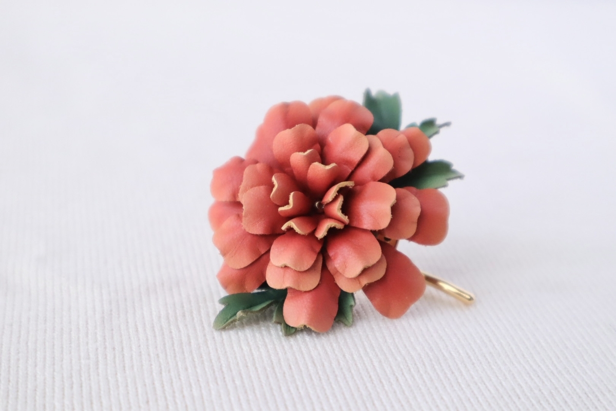 マリーゴールドの革花ポニーフック。手染めされた本革で作られた繊細な花が、温かみのあるオレンジ色で美しく仕上げられています。