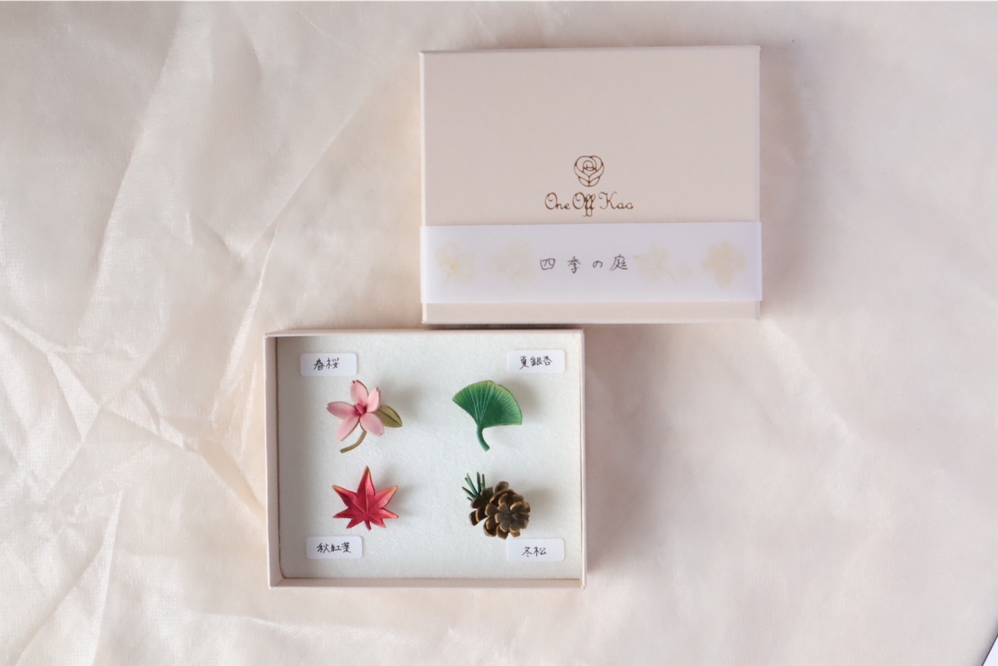四季の庭タックピンセット。帯に「四季の庭」と書かれたブランドボックスと、春桜、夏銀杏、秋紅葉、冬松の4つのタックピンが美しく並んだ状態。