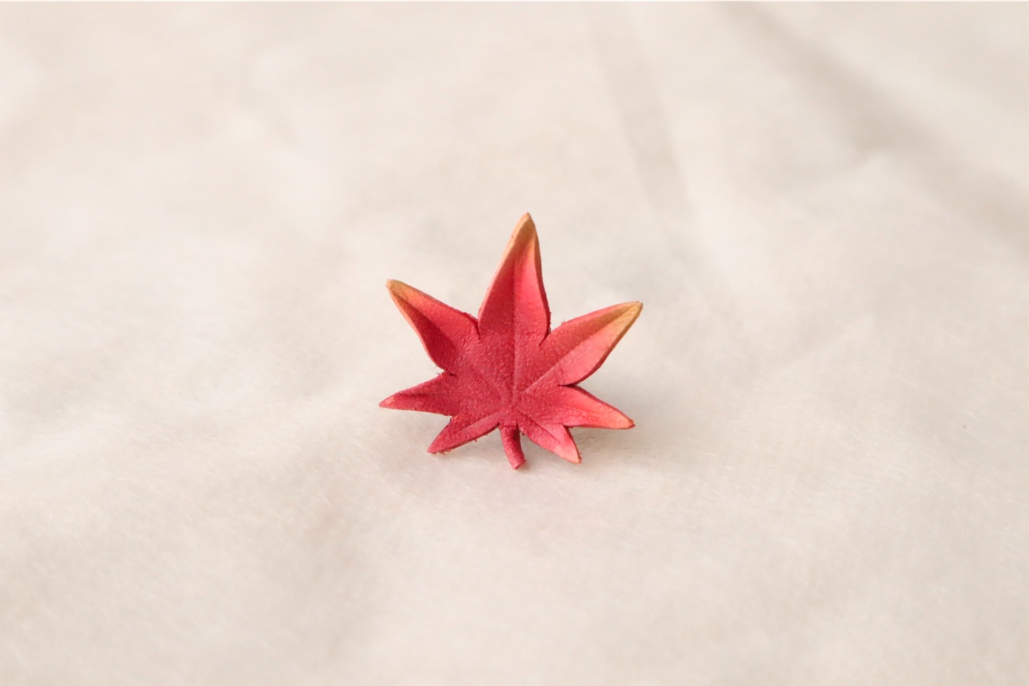 秋の紅葉をモチーフにした革製のタックピン。淡い赤とオレンジの色合いが印象的。