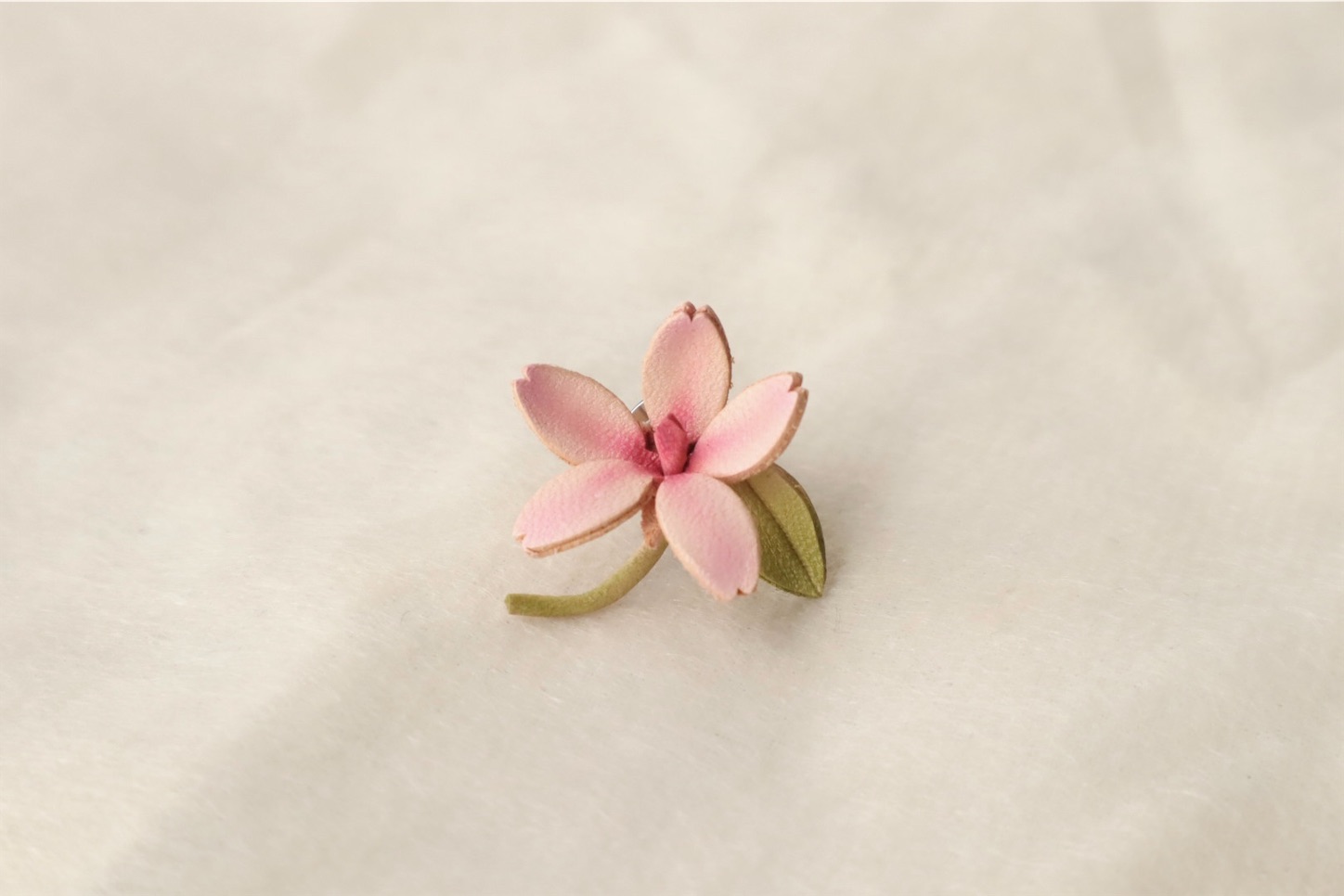 春の桜をモチーフにした革製のタックピン。淡いピンクの花びらが美しいデザイン。
