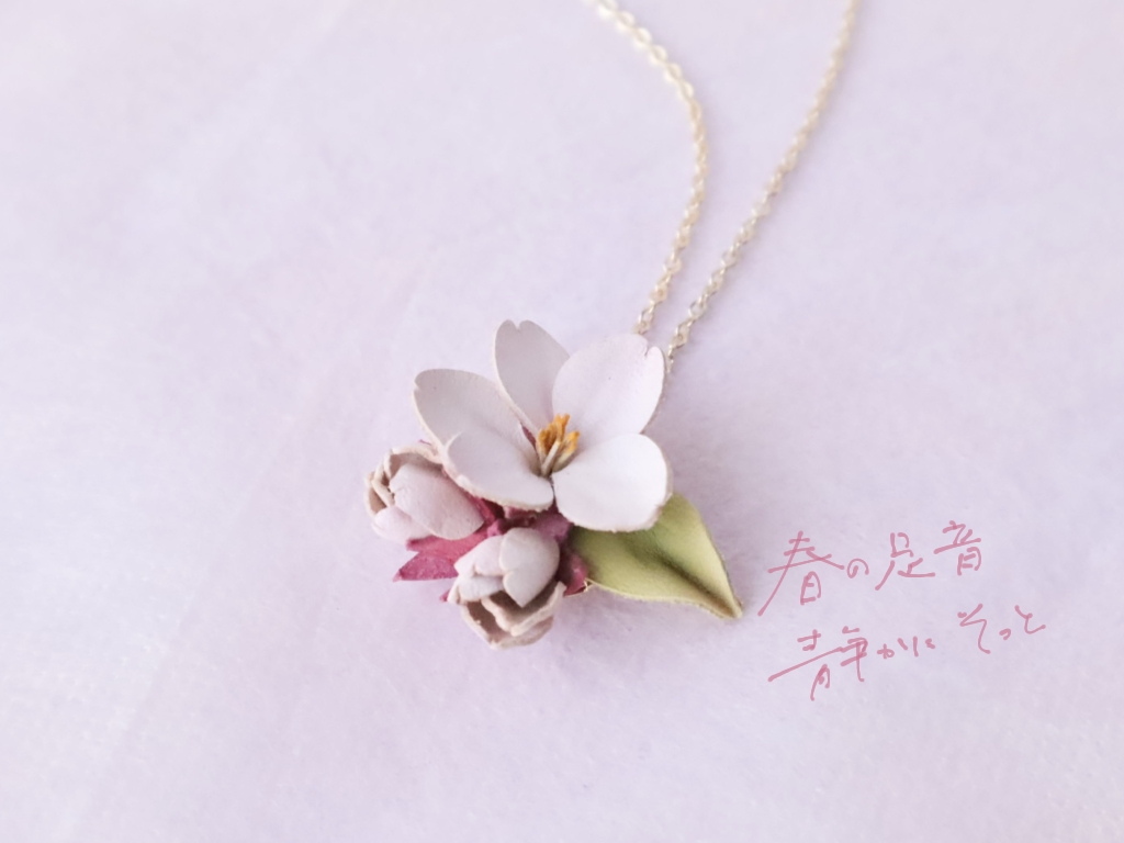 革で作られた桜のネックレスの画像。柔らかなピンクの花びらと、小さな蕾や葉が組み合わさった、春を感じさせるアクセサリー。
