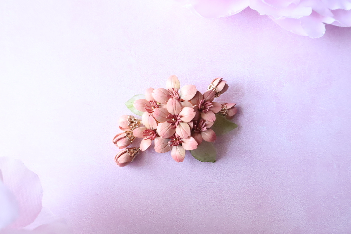 革で作られた2024年版の桜ブローチの画像。淡いピンクの花とつぼみ部分のゴールドの装飾が華やか。