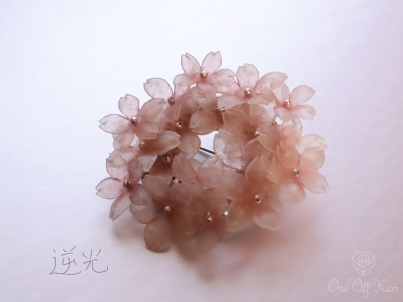 逆光で撮影された生革の桜ブローチ。光を透かして透明感が強調される。