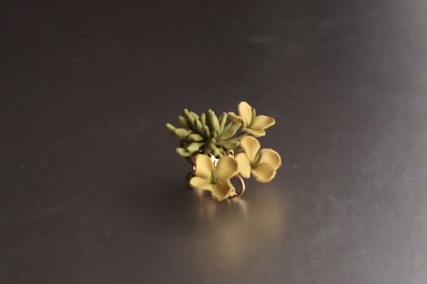 横から見た菜の花の革花イヤリング。緑の茎と花びらが立体的に作り込まれている。