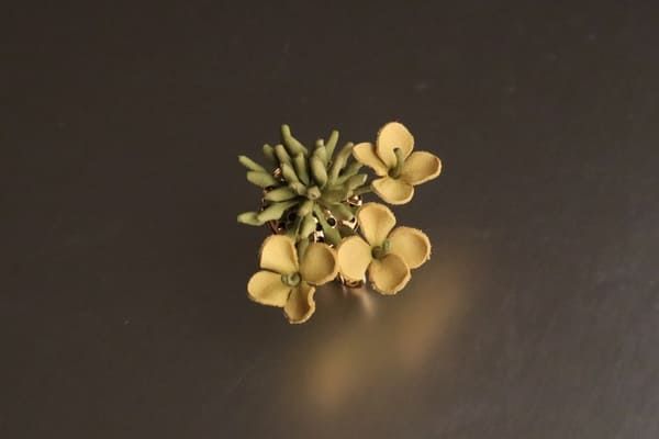 斜めから見た菜の花の革花イヤリング。黄色い花と緑のつぼみが配置されたデザイ斜め