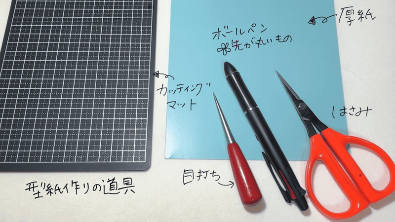 型紙作りに必要な道具一式。カッティングマット、厚紙、先が丸いボールペン、目打ち、はさみが並んでいる。手書きで「型紙作りの道具」と説明あり。