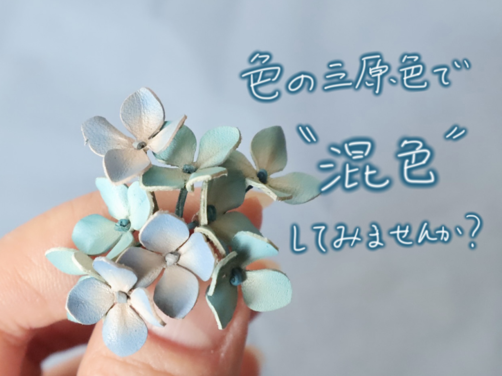 革で作られたあじさいの花を手に持った写真。やわらかなブルーのグラデーションで染められており、右側に「色の三原色で“混色”してみませんか？」という手書き風文字が添えられている。