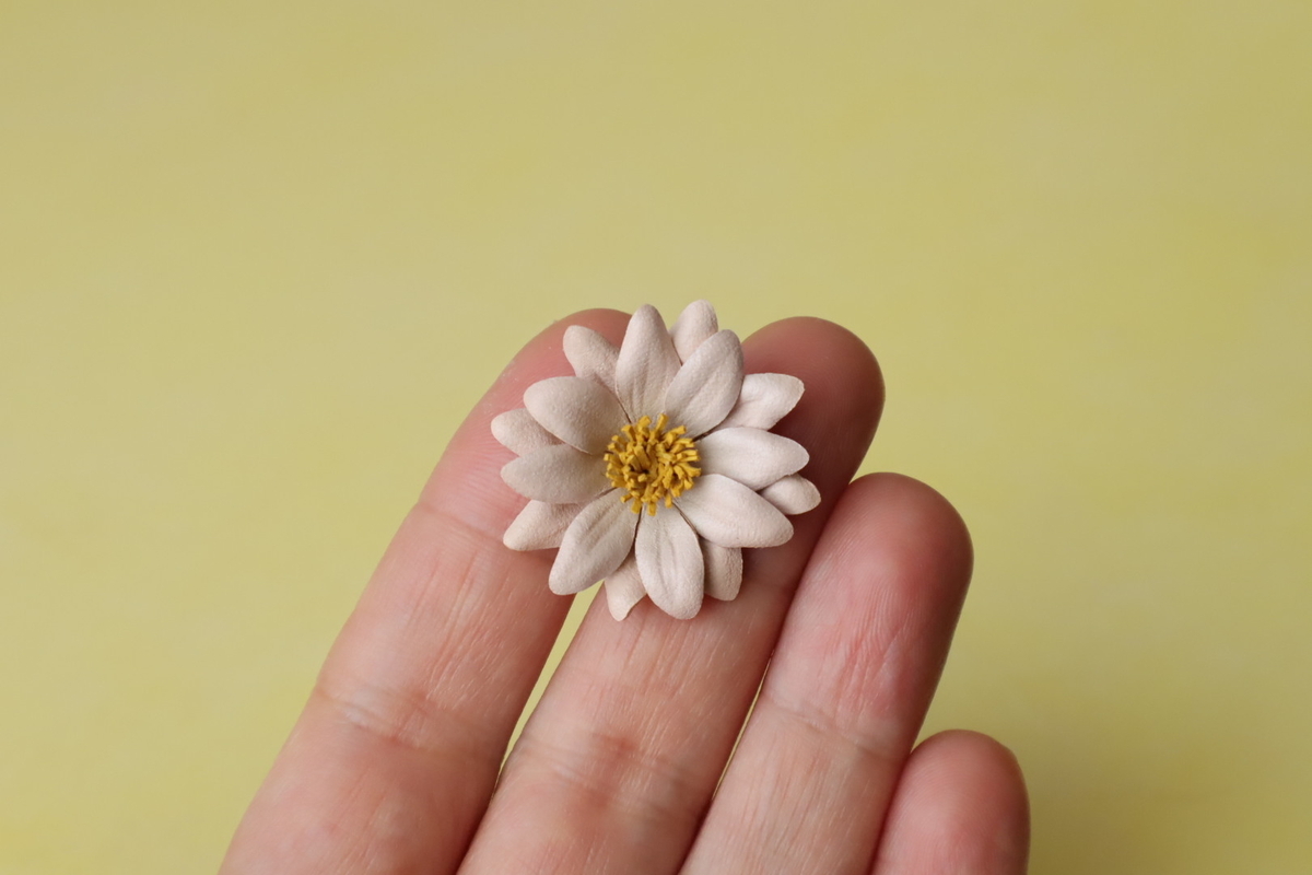 明るい背景に、革で作った小さなマーガレットを手に載せた画像。
