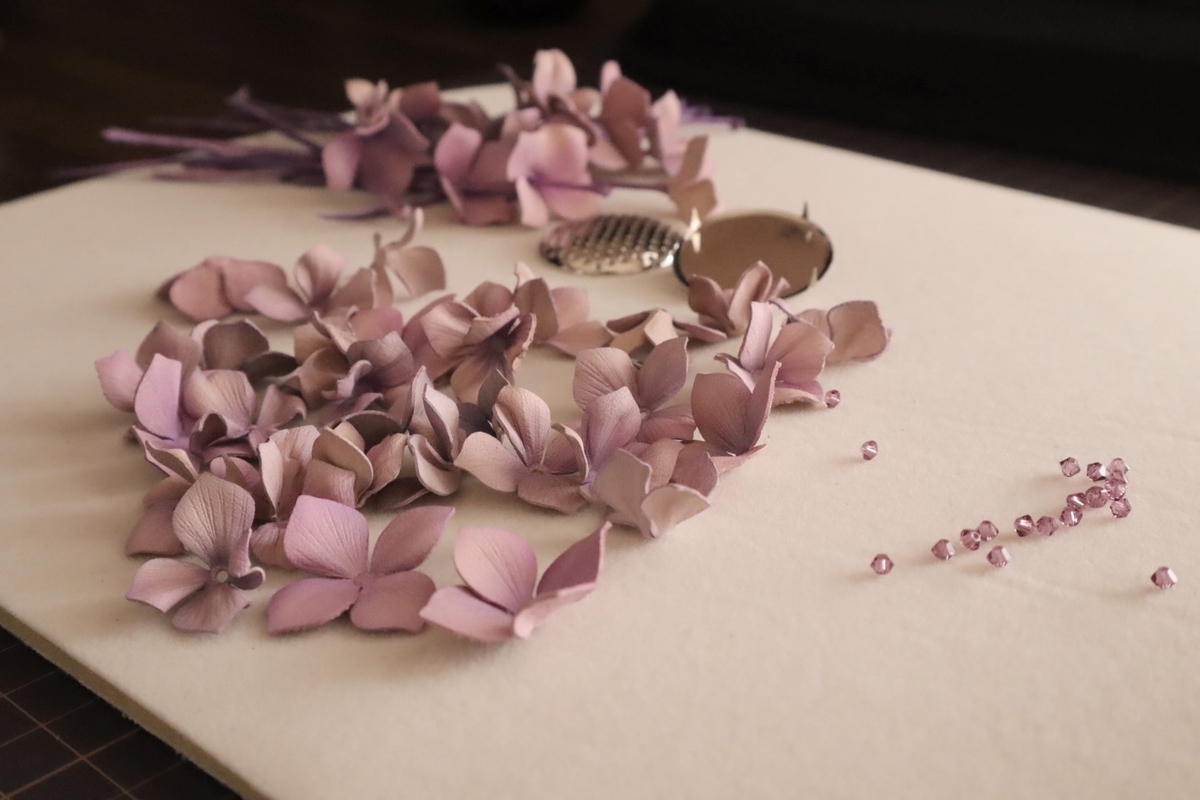 紫陽花ブローチの制作過程。染めた花びらが並べられ、中央にはブローチ台座と装飾用のビーズが配置されている。淡い紫色の花びらが美しく広がり、繊細な雰囲気を醸し出している