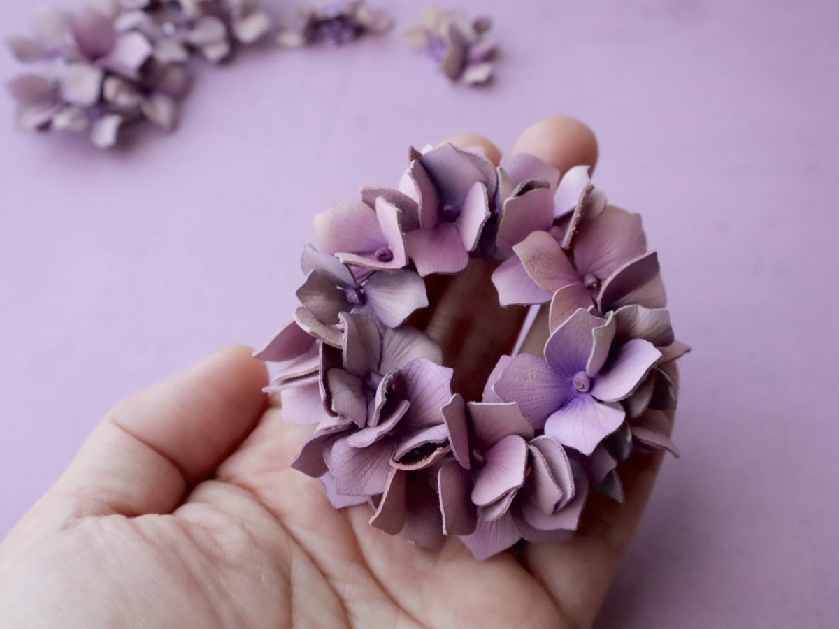 淡い紫色の革花アクセサリーを手に持つ様子。紫陽花の大輪がふんわりと咲き、柔らかな色合いが名残惜しさと温かさを感じさせる。