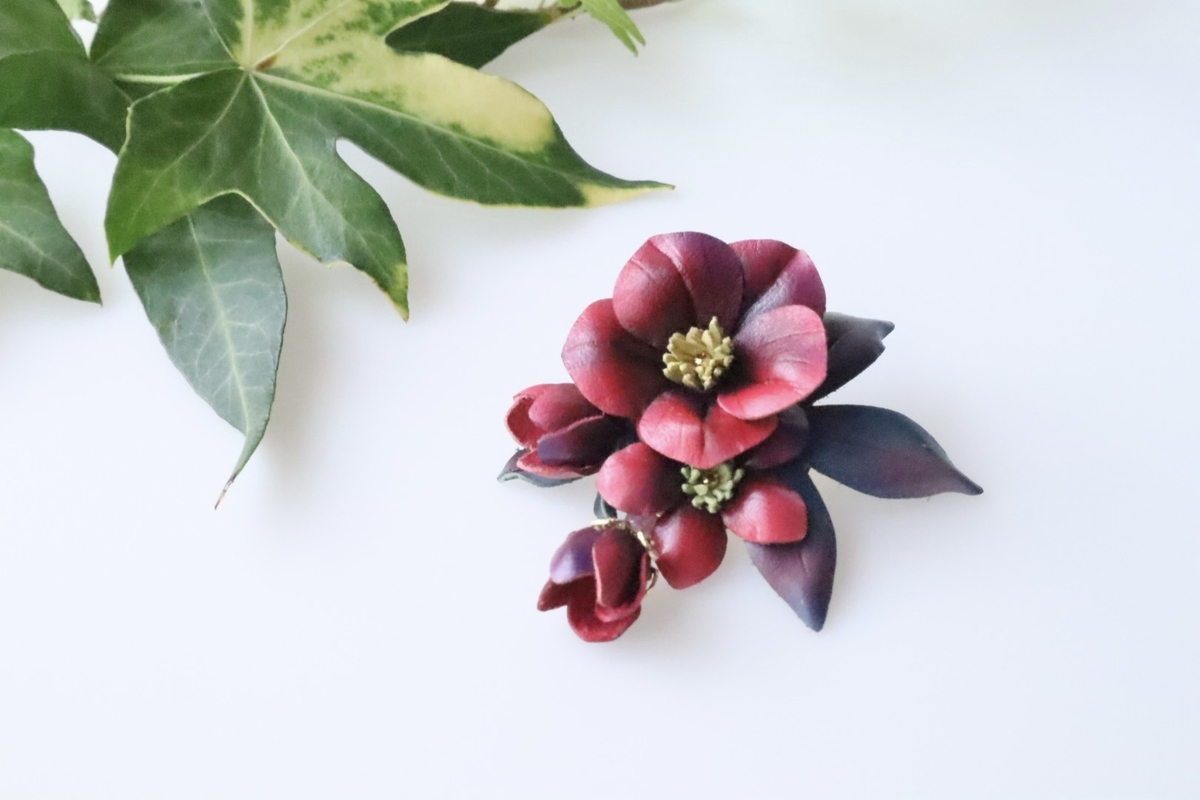 クリスマスローズをモチーフに作られた革花ブローチ。濃い赤を基調とした色合いで、数色の美しいグラデーション染めが施されている。