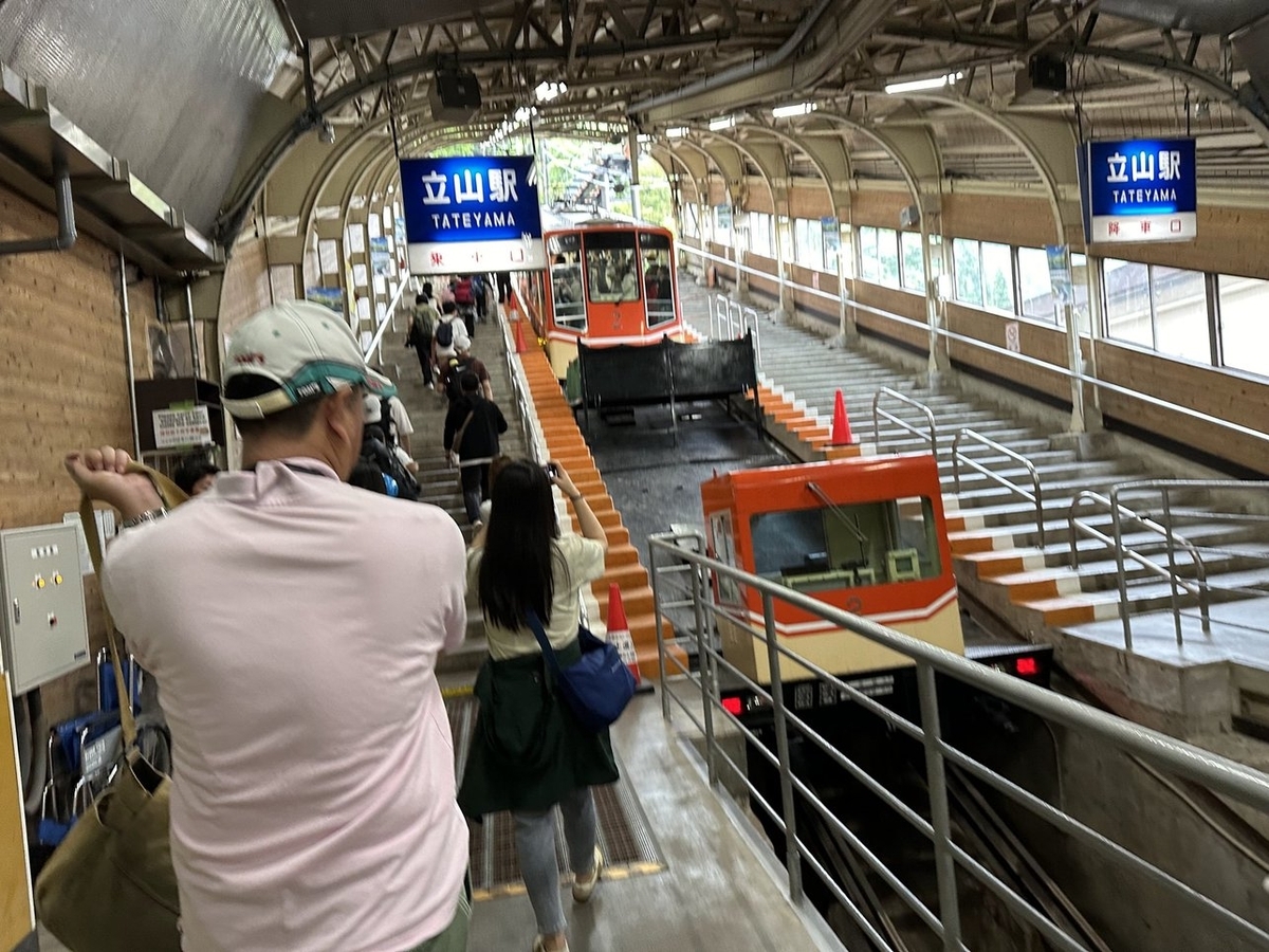 2つの階段の真ん中にケーブルカーがある。左の階段の上に「立山駅 乗車口」右に「立山駅 降車口」と表記された看板。