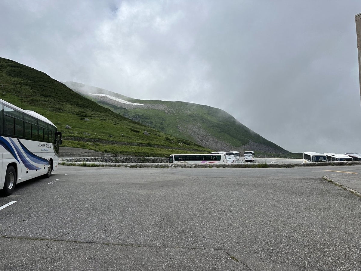 手前に道路、奥にバスの駐車場。左に一面みどりの山肌が見える