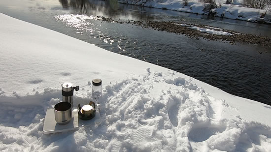 雪の川岸とコーヒーギアの写真