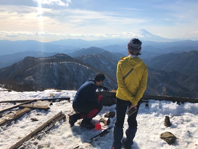 雪でアヒルを作る登山者を見ている山ガール