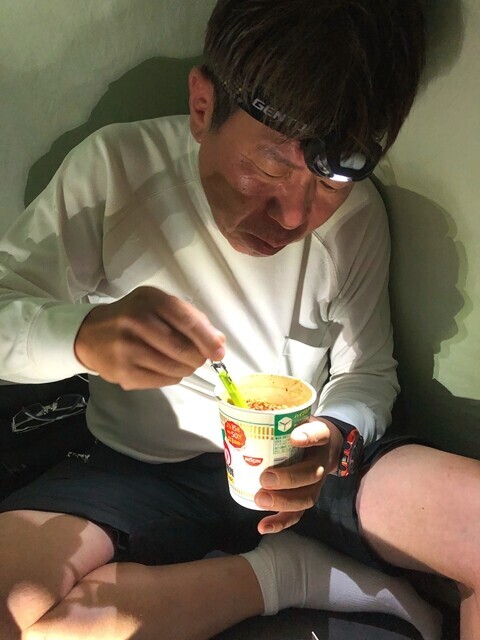 テントの中でカップ麵を食べている登山者