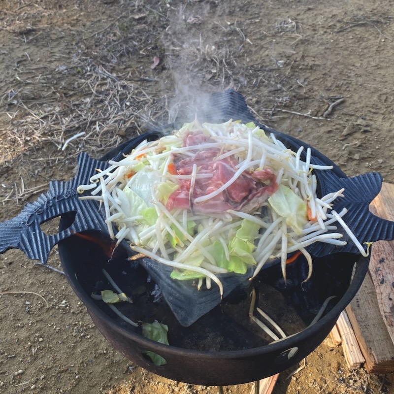 キャンプでジンギスカン鍋を使い生ラムを焼いている様子