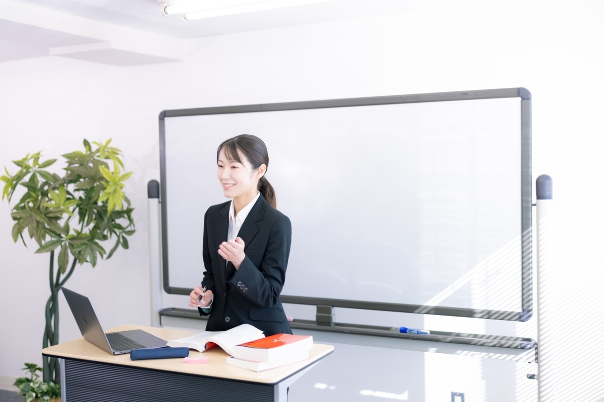 会社の会議室でホワイトボードを前に朝活でホワイト社会に適応する力についてプレゼンしている女性の画像