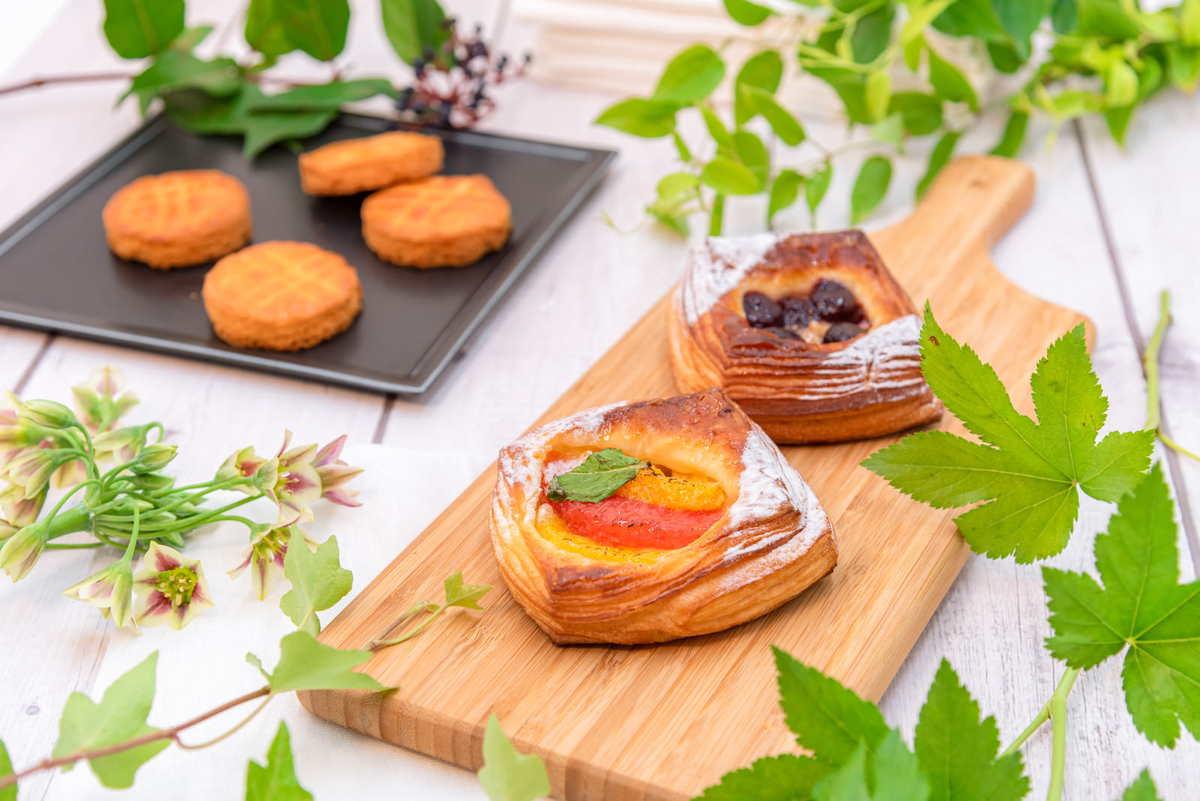 グリーンが添えられた木製のまな板の上に美味しそうなガレットやパイが置かれ、向こう側には焼き立てのクッキーが並べられている画像