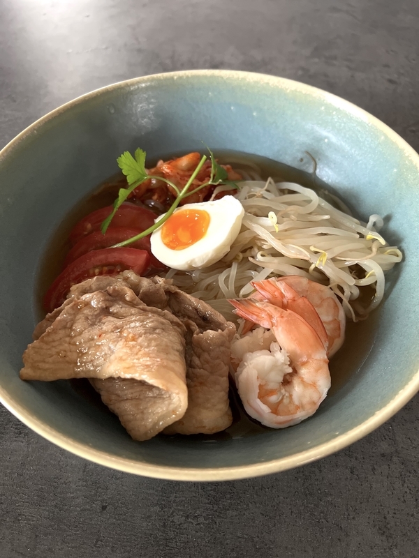 手作りのインスタント冷麺にえび、もやし、ゆで卵、焼肉用の肉、キムチ、トマトを盛りつけた写真