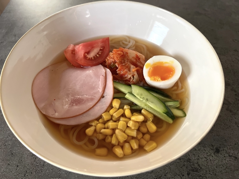 手作りのインスタント冷麺にきゅうり、トマト、ゆで卵、ハムを盛りつけた写真