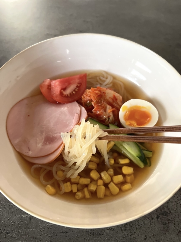 冷麺を盛り付けて、麺を箸で持ち上げている写真