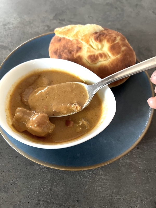 セブンイレブンの冷凍バターチキンカレーと冷凍ナンを盛り付けてカレーをスプーンですくっている写真