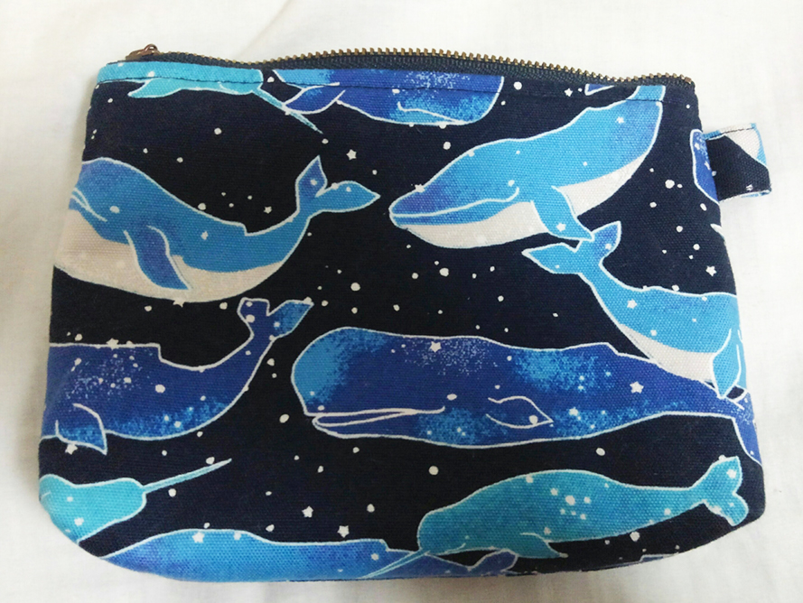 深い海のような紺色の布に鮮やかな青や水色のクジラが泳ぎ無数の星が散らばった柄の布で作られたチャック式のポーチ