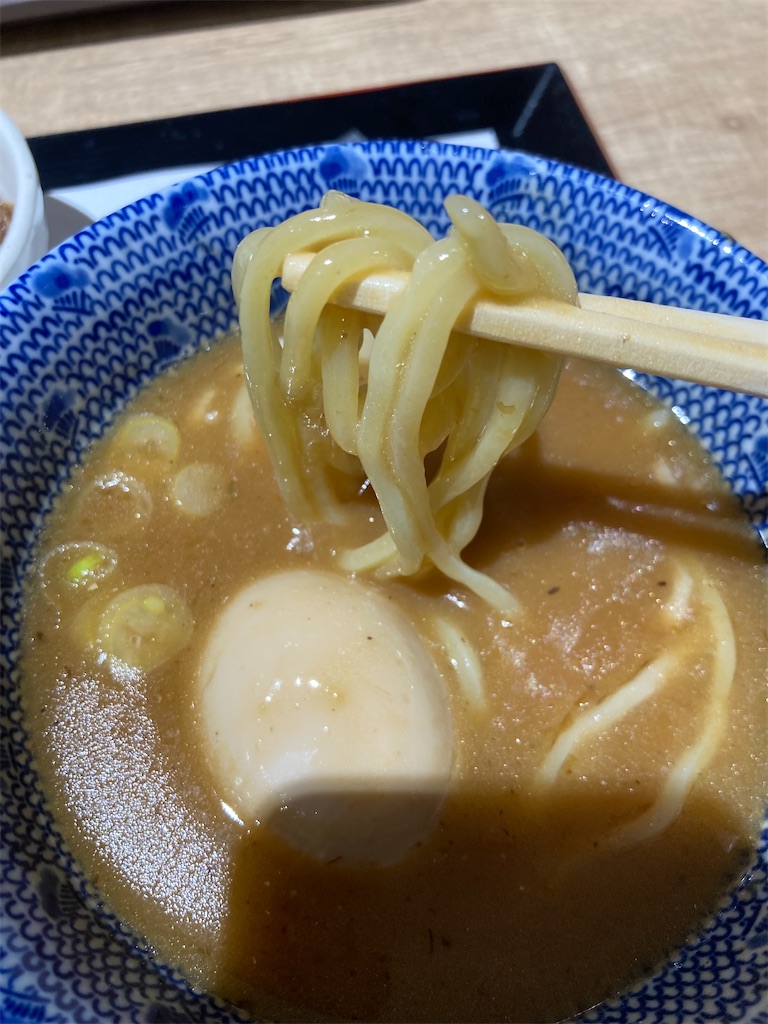 厚みのある麺を箸で持ち上げ、濃厚なつけ汁に浸している様子。つけ汁の中には半熟卵が浮かんでいる。