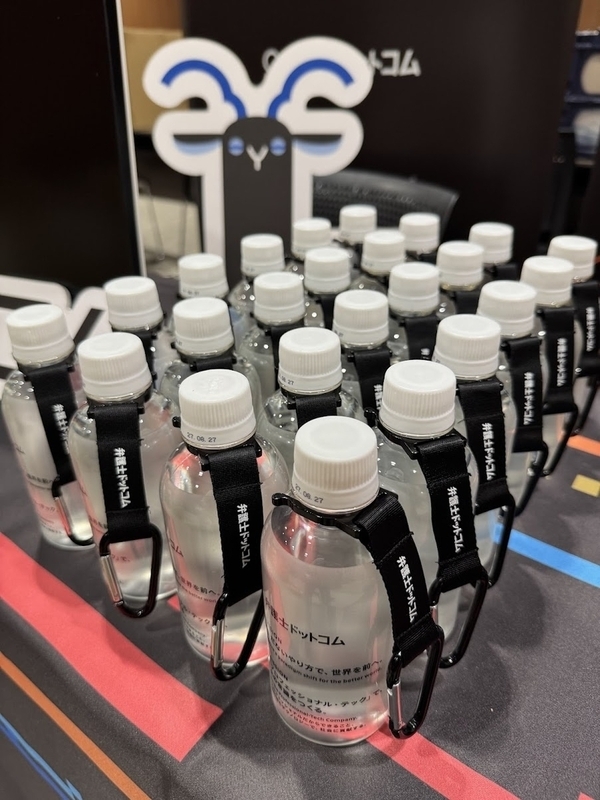 ノベルティの水。350mlのペットボトルと、ペットボトルホルダーがセットになっている。ボトルには弁護士ドットコムの社名ロゴと、各種スローガンが書かれている