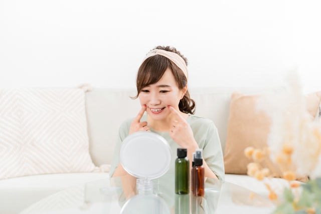 鏡を見ながら最近、肌の調子が整ってほうれい線が消えてきたと感じているメイク中の女性