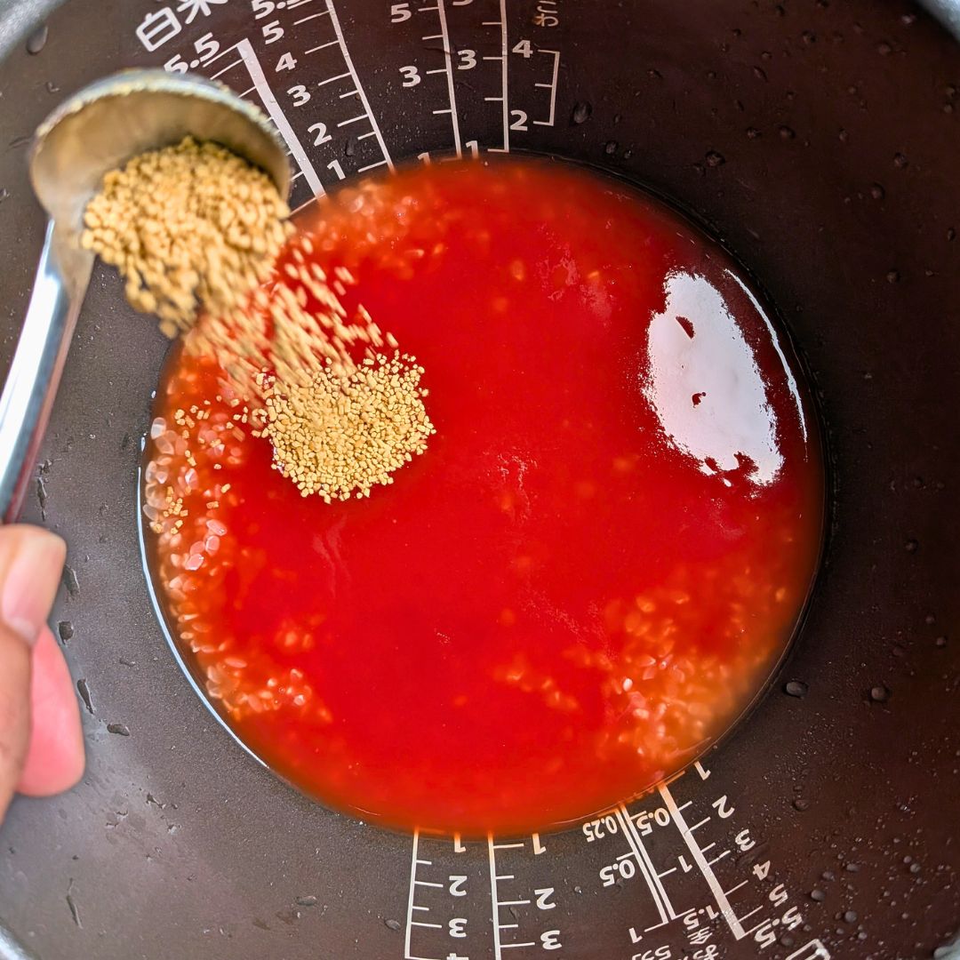 炊飯器に米とトマトジュース、コンソメを入れて水加減を調整する様子