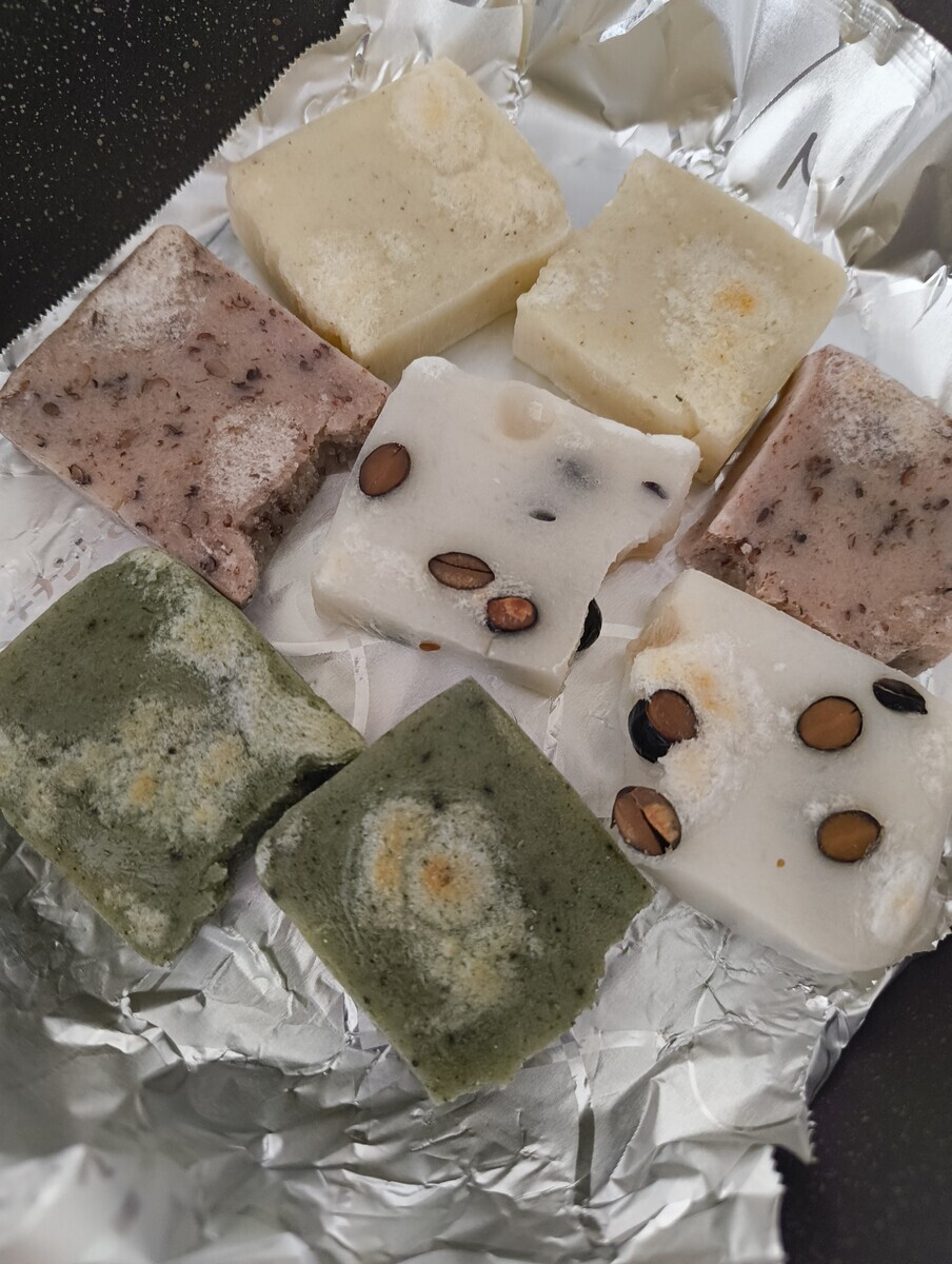 アルミホイルの上で焼かれている斗棒餅の写真。黄色い餅、赤茶色の餅、黒豆が入った餅、よもぎ色の餅。