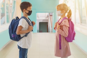 外国の学校での廊下で向かい合わせに立つマスクをした男の子と女の子