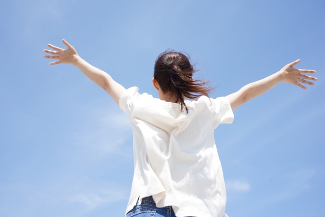 青空に両手を広げる女性